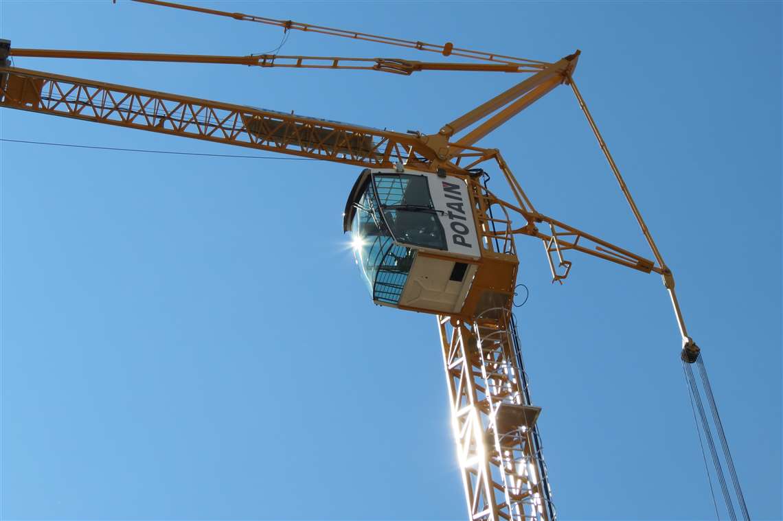 yellow Potain tower crane against a blue sky