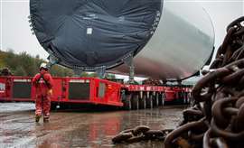 big white turbine tower section on a red Mammoet self propelled modular transporter with the power pack unit in the foreground