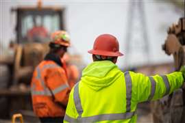 Image of two construction workers in hard hats with their backs to the camera and a piece of construction machinery in the background.