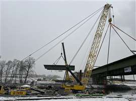 The floating crane holds the weight of the larhe bridge section while the onshore crane hoists a smaller section away. 