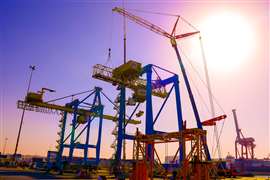 Big 400 tonne Liebherr with lattice jib lifting old container crane components against a bright sky