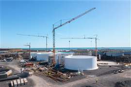 big Liebherr self erecting tower cranes assembling large white cylindrical tanks for Atlantic salmon