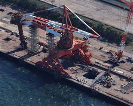 Aerial view of large red and white ship unloader crane at JFE Steel in Kawasaki, Japan, with missing counterweight and large hole in quayside where it punched through as it fell