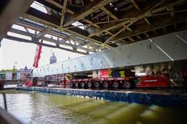 A steel deck section is transported beneath the existing bridge structure on a flat-top barge at Amsterdam Centraal Station. Photo: Mammoet