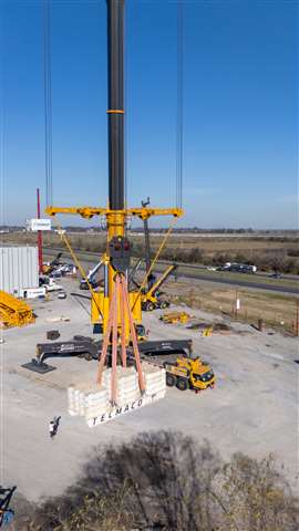 La grue jaune XCA3000 soulève un grand plateau blanc de plaques de contrepoids.