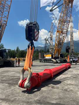 Ein großer roter Hebebalken hängt mit großen Bügelschäkeln und kurzen orangefarbenen Faserschlingen an zwei Liebherr-Raupenkränen.