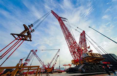 Red, yellow and black giant Sany crawler side view lifting something against a blue sky